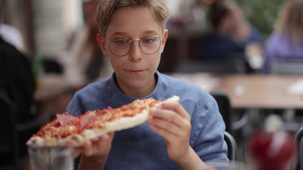 小男孩在餐馆里吃着美味的意大利披萨。视频素材