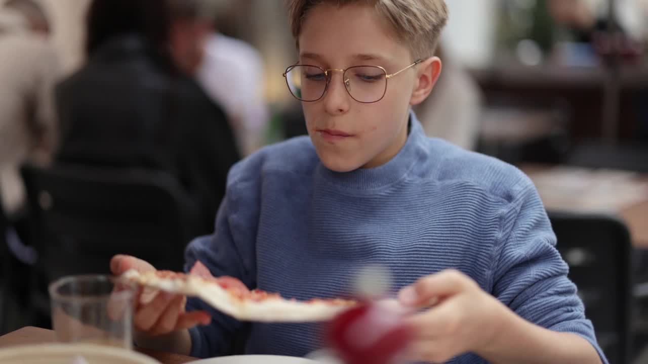 小男孩在餐馆里吃着美味的意大利披萨。视频素材