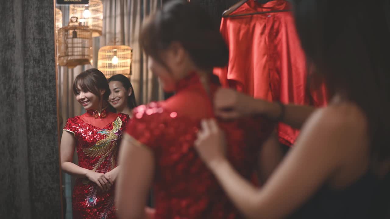 在传统精品店，一名亚洲华人女子在姐姐的帮助下，对着镜子试穿中国传统旗袍视频下载