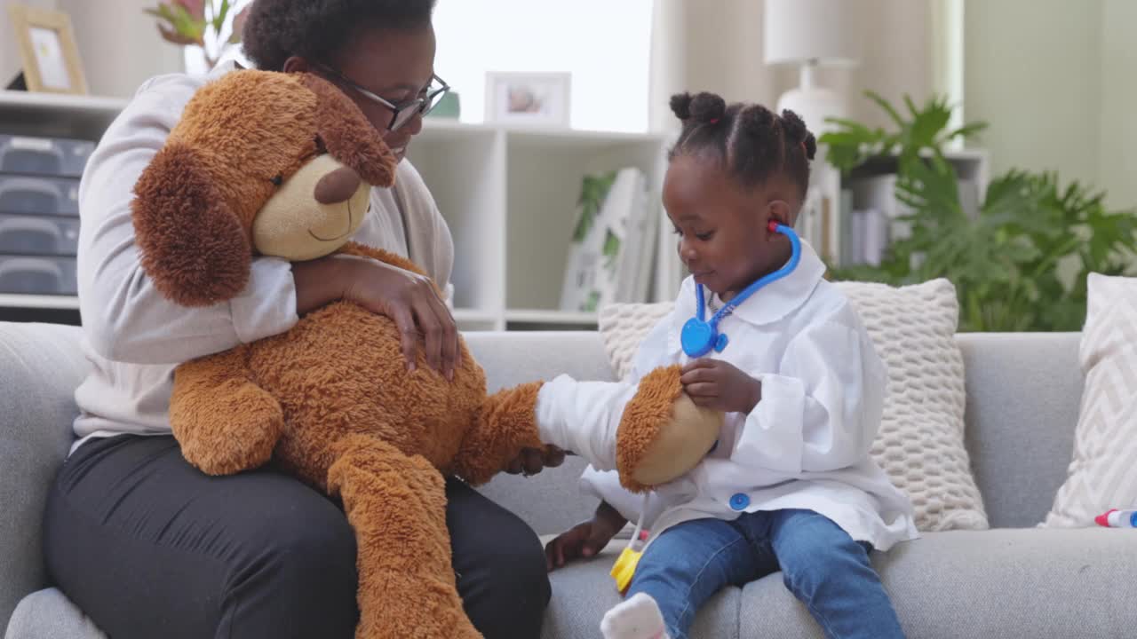 4k视频记录了一个小女孩穿着医生服在家里和她的妈妈和泰迪熊玩耍的画面视频素材