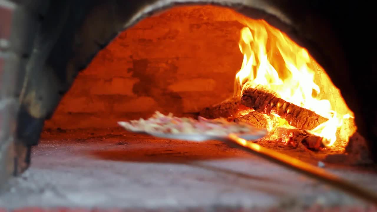 用燃烧的火焰在传统的比萨饼烤炉中烘烤比萨饼视频素材