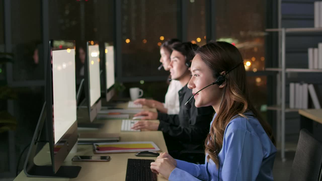 热线接线员。呼叫中心的员工晚上在现代化的办公室里使用电脑和耳机视频素材