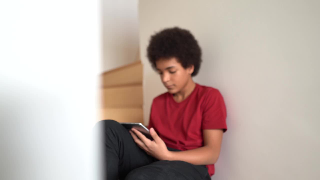 一个十几岁的男孩坐在楼梯上使用数码平板电脑视频下载