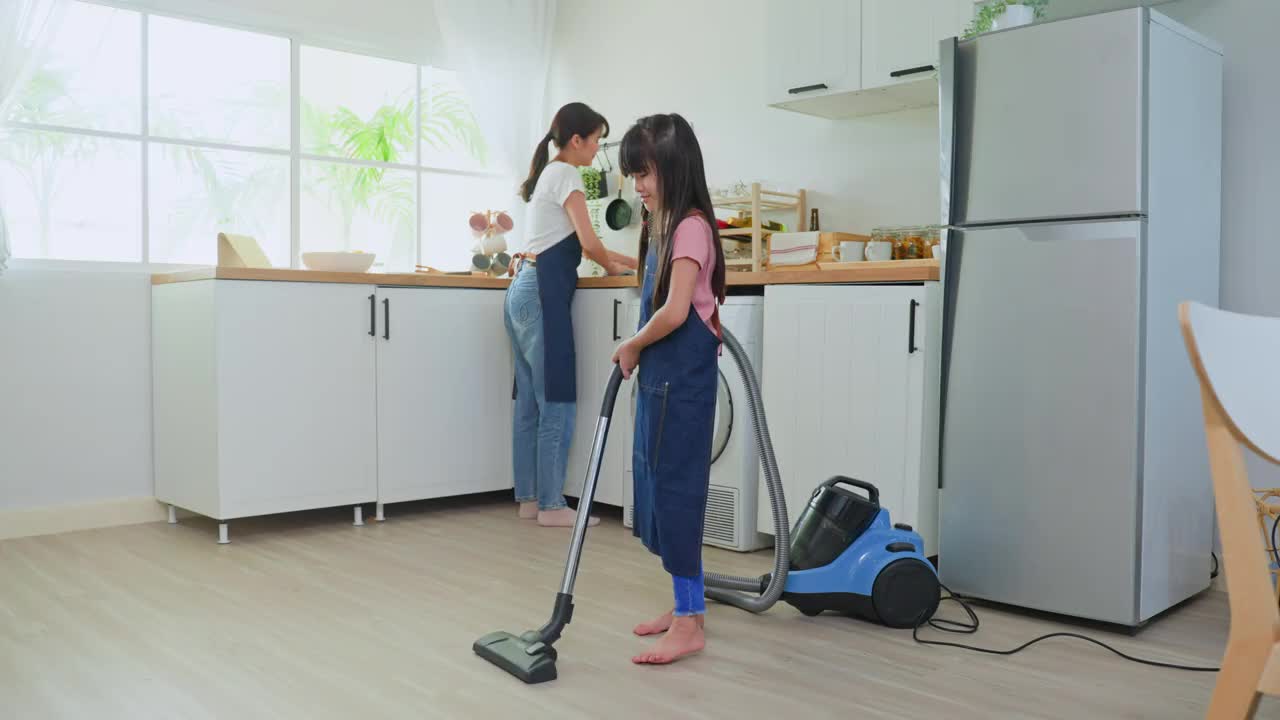 亚洲漂亮的母亲教小女孩打扫厨房在家里。爱美丽的父母妈妈帮助和支持小女儿在家打扫房间的地板。活动关系的概念。视频素材