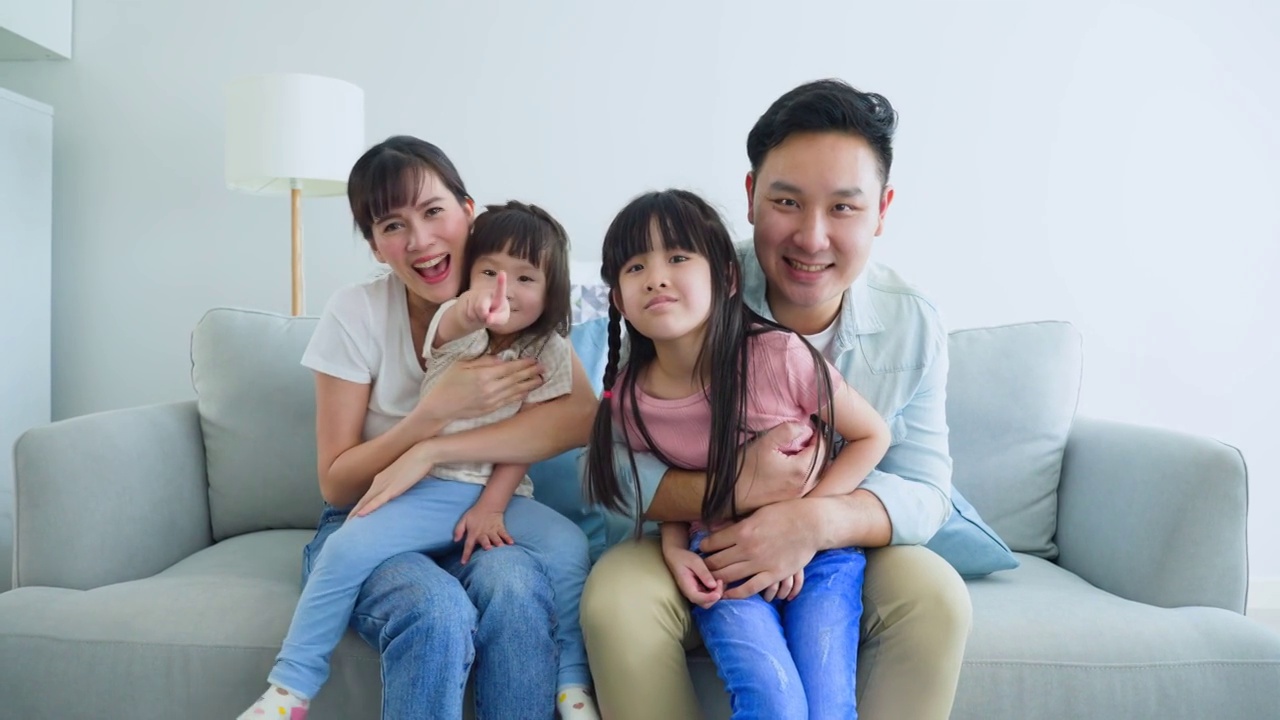 亚洲幸福家庭的肖像花时间与孩子一起在家里。年轻可爱的小女孩和父母坐在沙发上微笑着，看着摄像机在客厅里。活动关系的概念视频素材