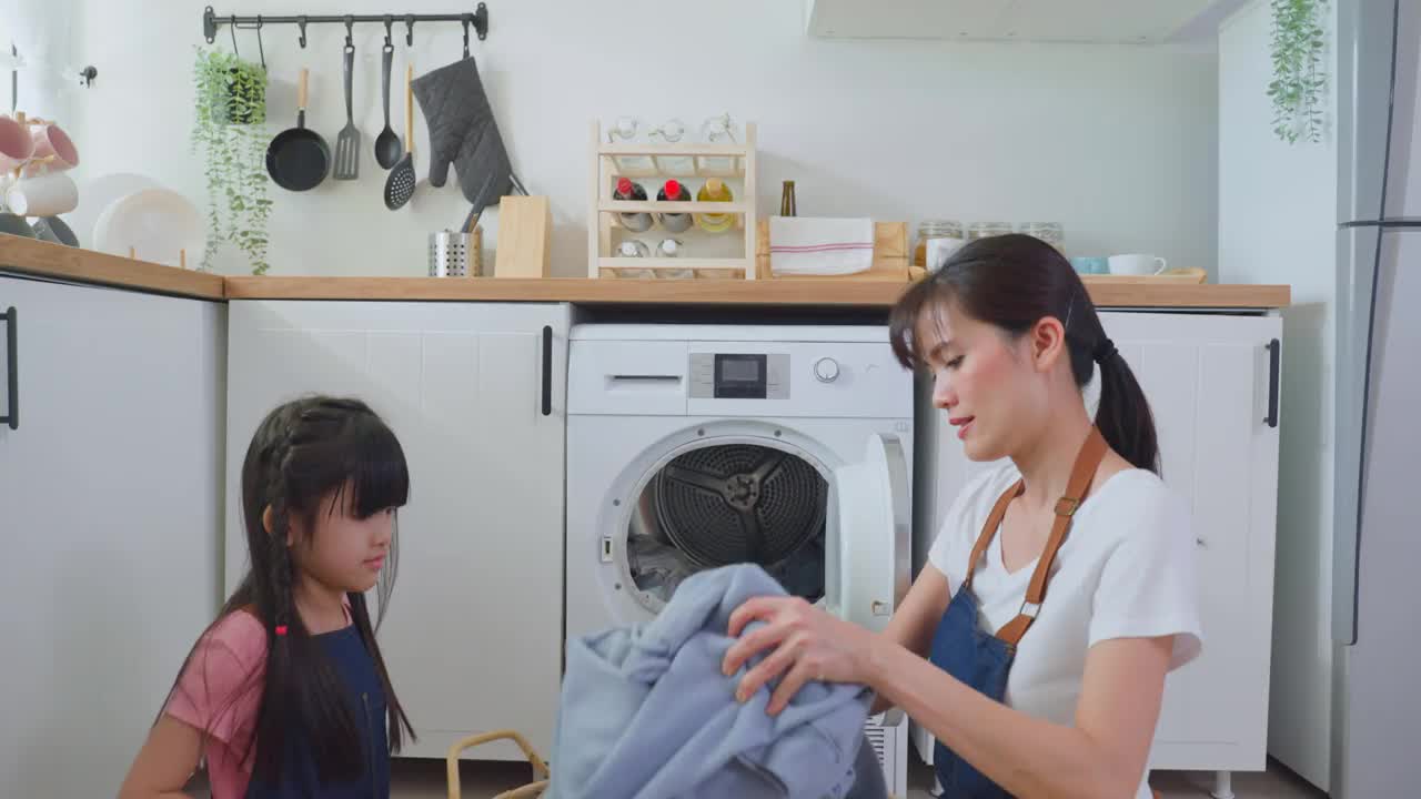 亚喜一家人待在家里，妈妈教女儿洗脏衣服。年幼可爱的小女孩帮助父母妈妈把衣服放在家里的洗衣机里。Domestic-Housekeeping。视频素材