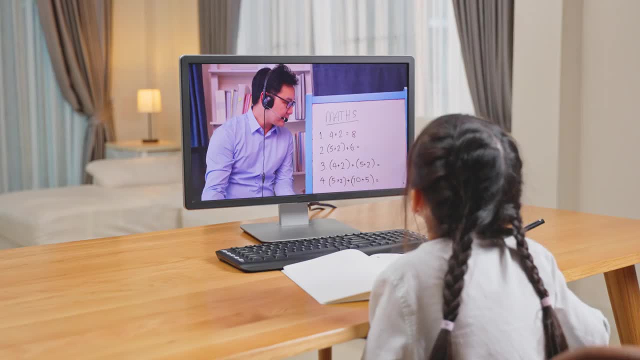 亚洲年轻女孩在网上看虚拟视频，在家里用笔记本电脑学习。由于covid - 19大流行，在家上学的孩子使用电脑学习，并通过数字远程会议听取学校老师的意见。视频素材