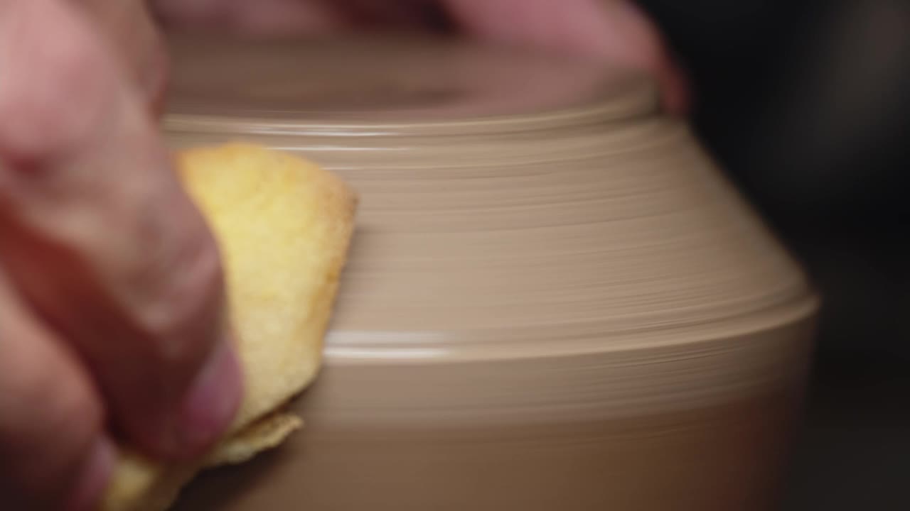 陶工的手用黄色海绵擦拭陶工转盘上旋转的粘土制品。宏射击视频素材