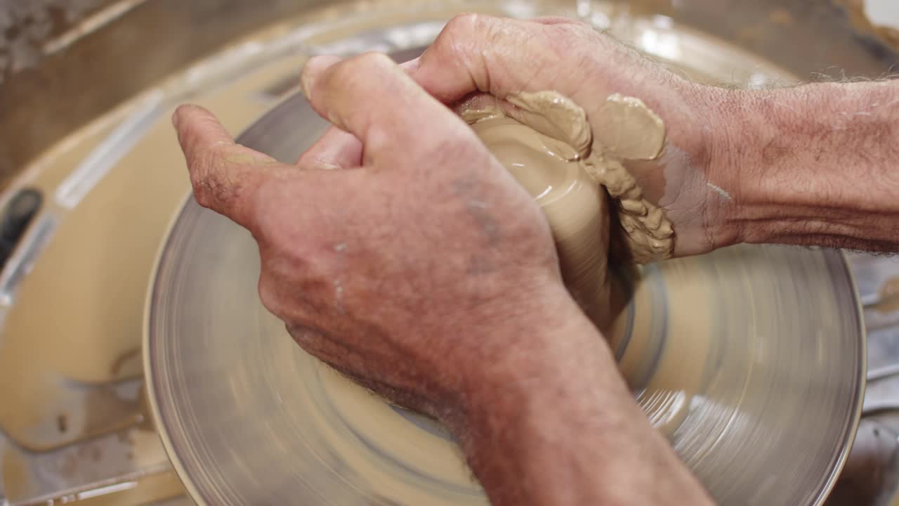 熟练的陶工在陶轮上转动粘土，使其拉长形状。手的特写，侧视图。制作陶瓷餐具的概念视频素材
