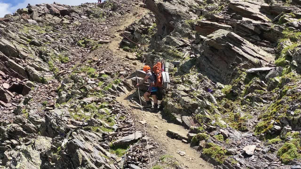 一名游客抓住垂直栏杆上的绳索，沿着山路从悬崖上下来视频下载