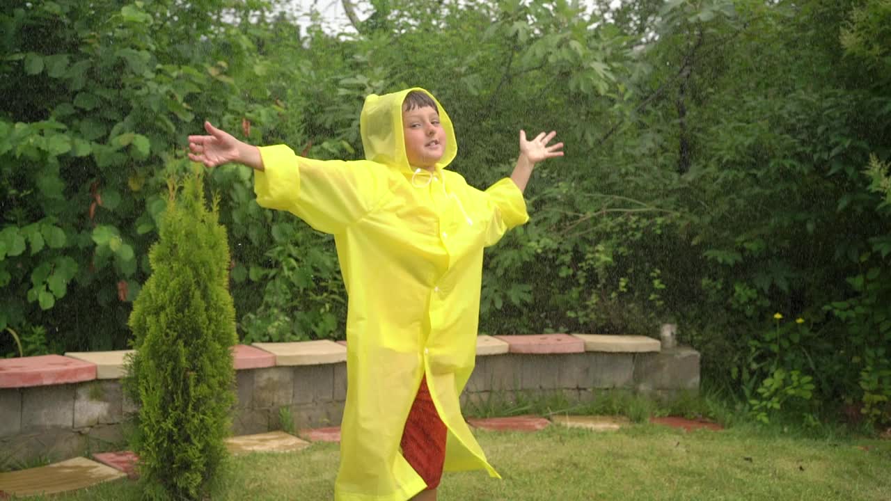 有趣的快乐男孩举起手，穿着黄色雨衣，在下雨的时候跳舞视频下载
