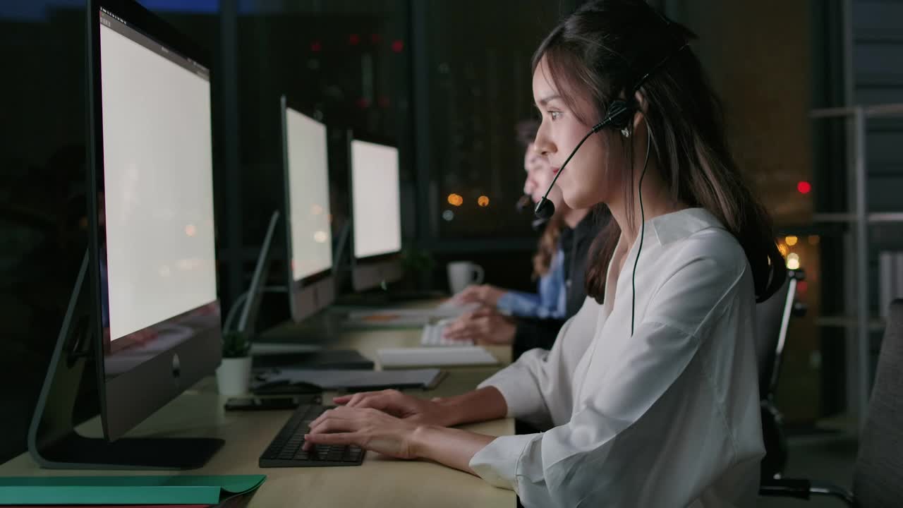 热线接线员。呼叫中心的员工晚上在现代化的办公室里使用电脑和耳机视频素材