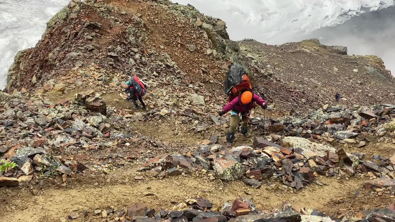一个疲惫的游客背着一个大背包，跌跌撞撞地沿着山路，经过巨石视频下载