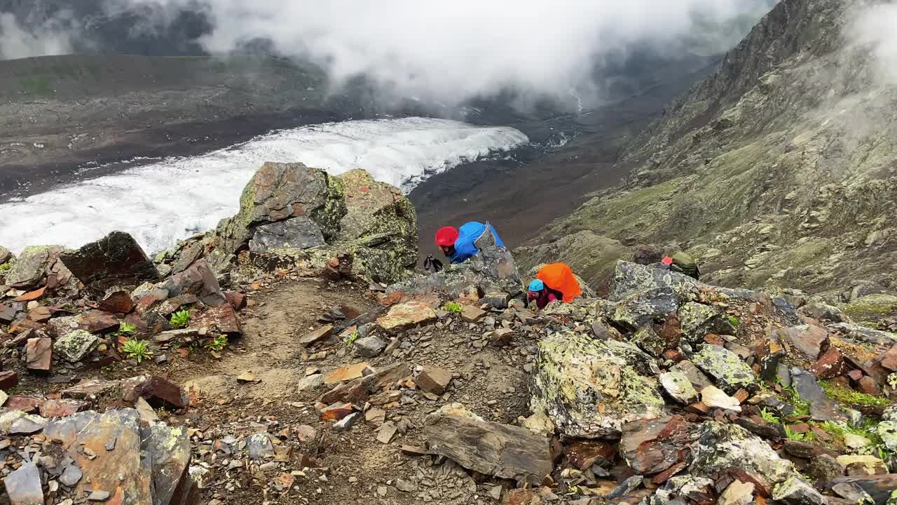 一个由三个游客组成的旅游团爬上一条山路，经过散落的石头和巨石视频素材