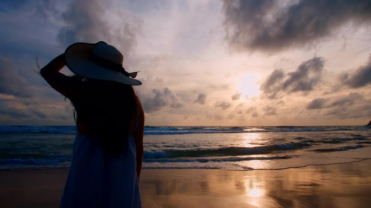 4K背景美女站在海滩上与海外的日落。快乐的女游客站在沙滩上，放松地欣赏日落。普吉岛，泰国自由天堂海滩。夏天假期的假期视频素材
