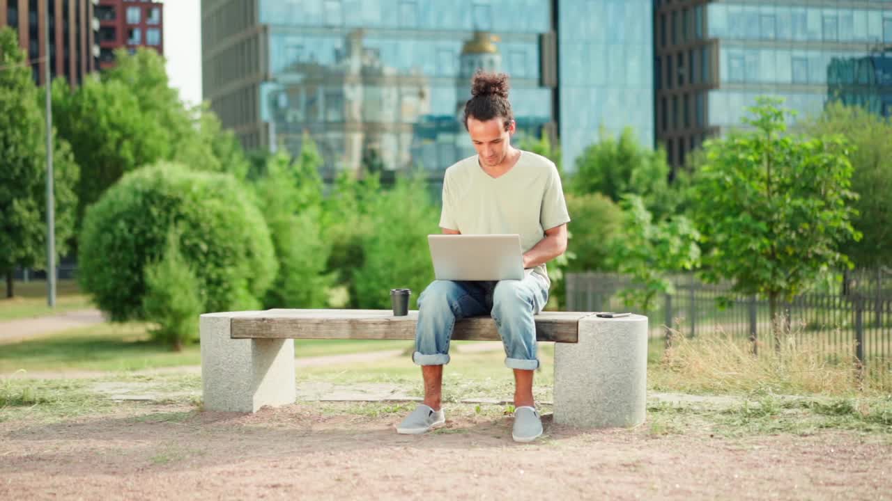 用慢镜头放大年轻人在笔记本电脑上远程工作，关上电脑，坐在户外长凳上思考。男性企业家，自由职业者或学生完成工作视频素材