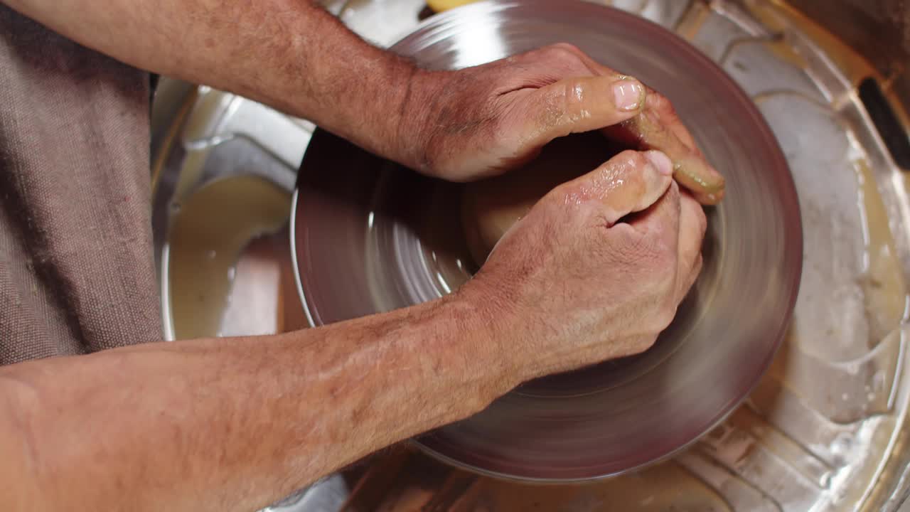 男陶工的手在陶工的轮子上转动粘土，给它想要的形状，俯视图。餐具制造中的创意和艺术概念视频素材