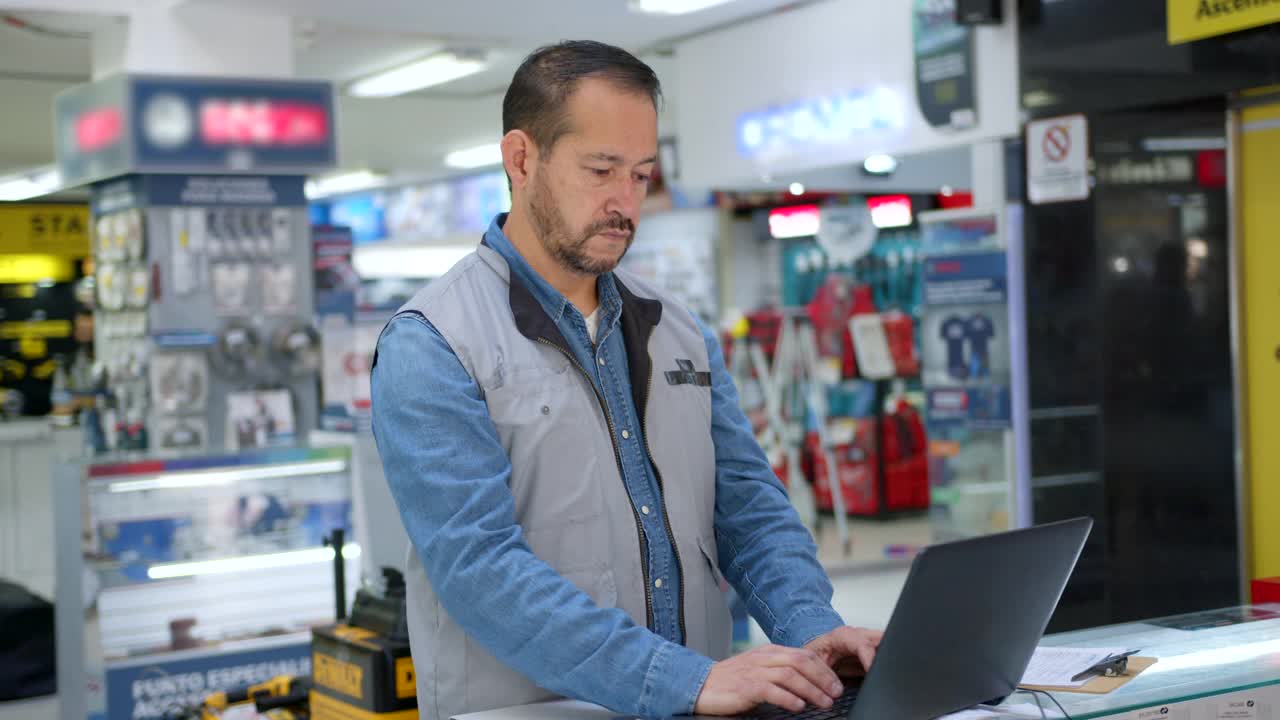 一个五金店的拉丁美洲主管，用笔记本电脑工作，然后非常愉快地面对着摄像机，微笑着视频素材