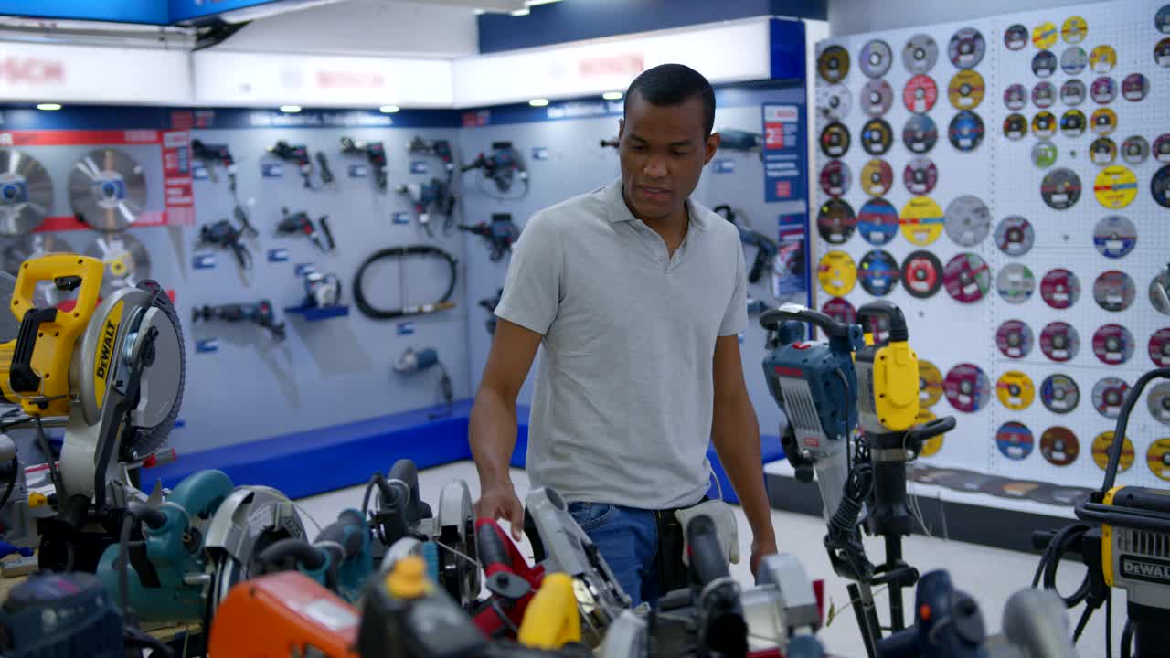 一位黑人男性顾客在五金店看不同的工具视频素材
