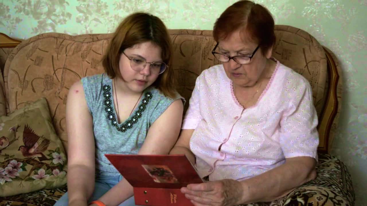 祖母给她的孙女看家庭相册里的旧照片。一个幸福的家庭。视频素材