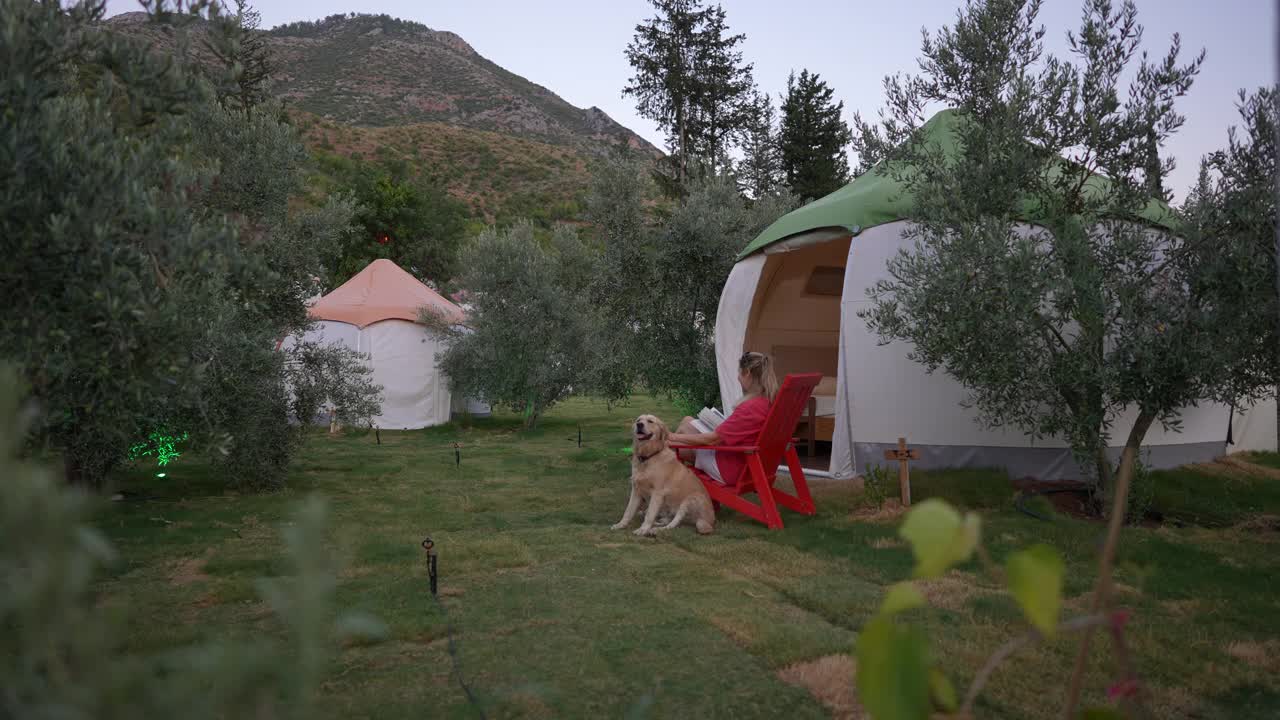 一个女人坐在豪华露营区，她的狗就在帐篷前。视频下载