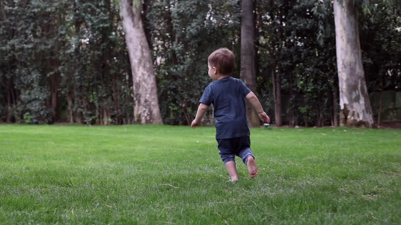 在温暖阳光灿烂的夏日里，小男孩赤脚在新鲜的青草上奔跑。侧视图。第一步之外视频下载
