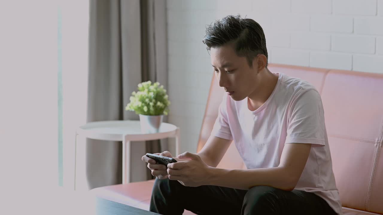 年轻的亚洲男子在智能手机上玩电子游戏视频下载
