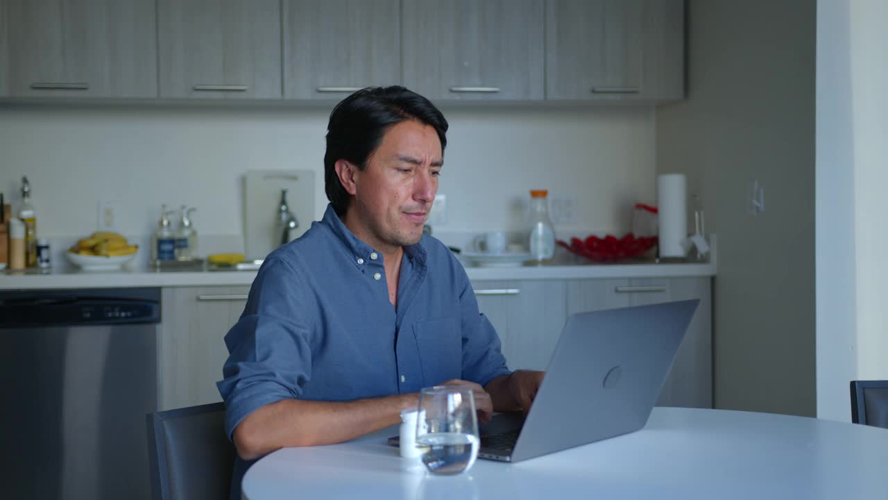 一名拉丁美洲男子在家里用笔记本电脑工作，看起来压力很大，正在吃头痛药视频下载