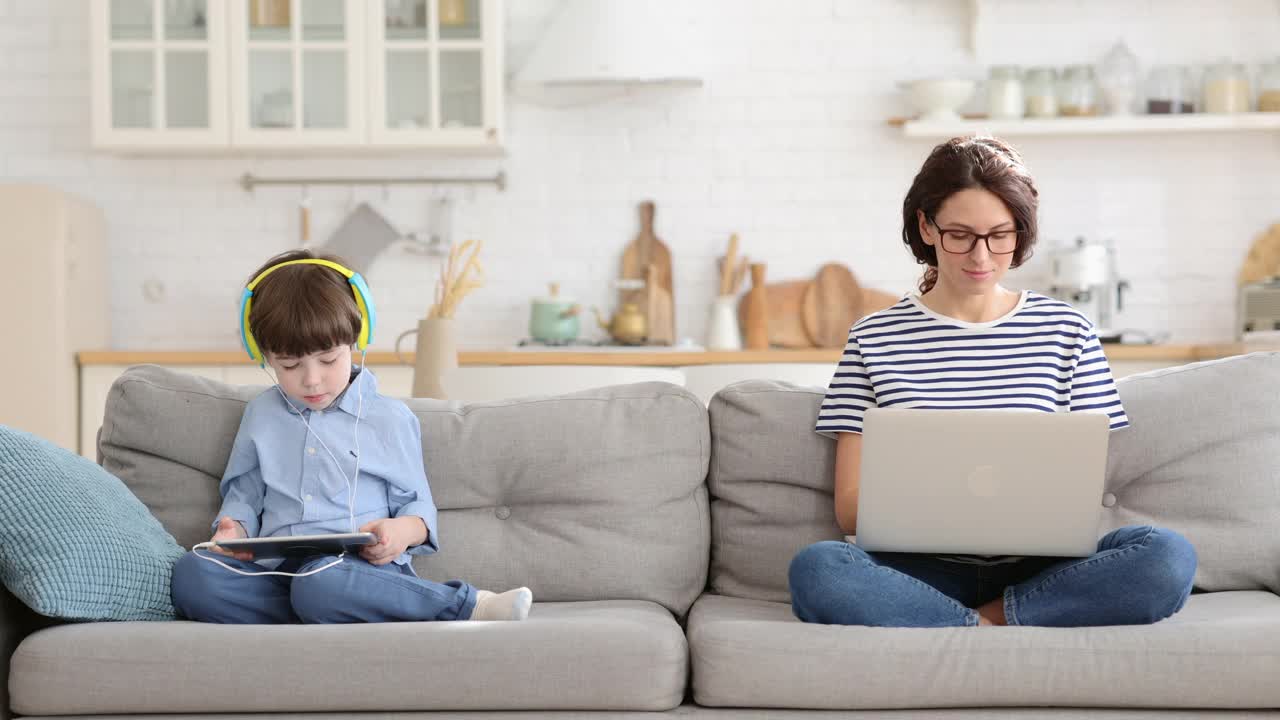 妈妈，自由职业者，远程工作，在家办公，坐在沙发上，孩子玩平板电脑。封锁视频素材