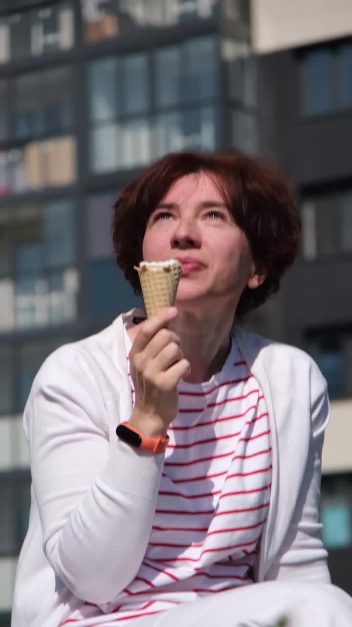 一个女人坐在城市街道的长椅上，享受着冰淇淋蛋筒视频素材