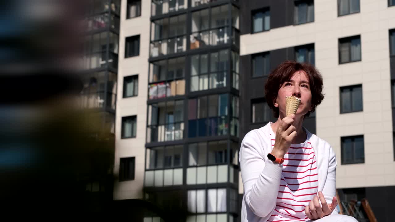 一个女人坐在城市街道的长椅上，享受着冰淇淋蛋筒视频素材