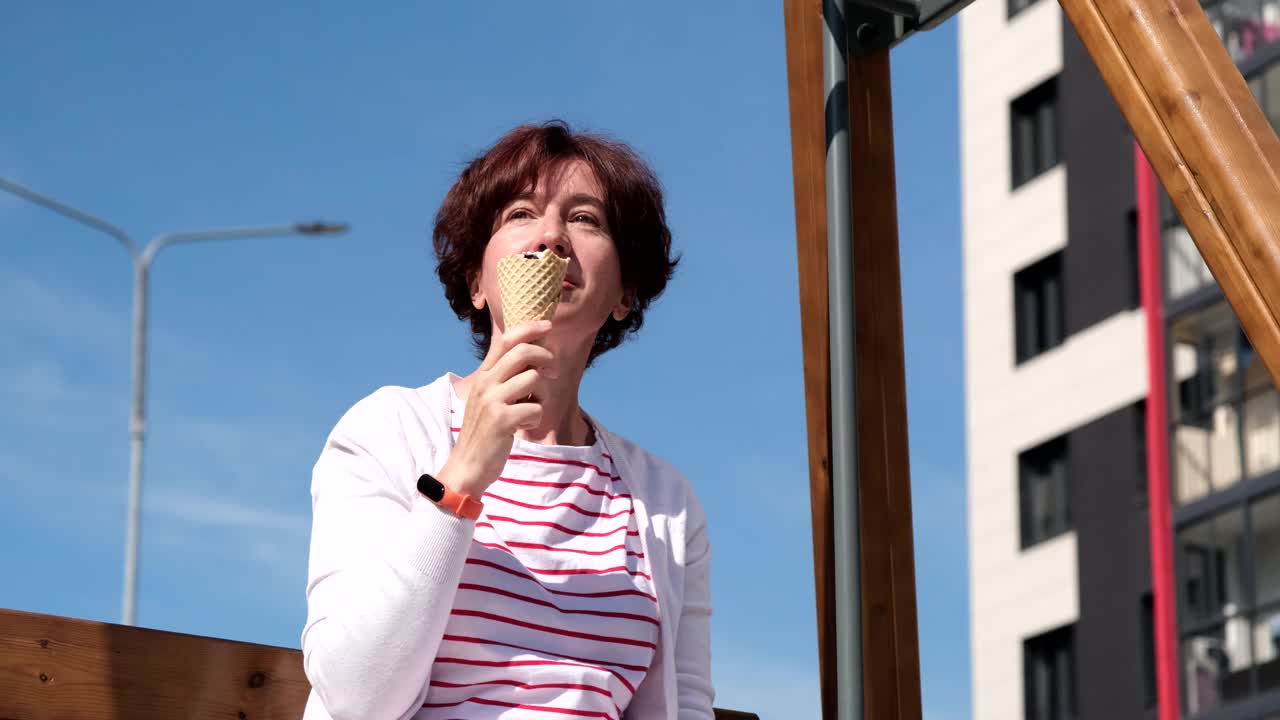 一个女人坐在城市街道的摇椅上，享受着冰淇淋蛋筒视频素材