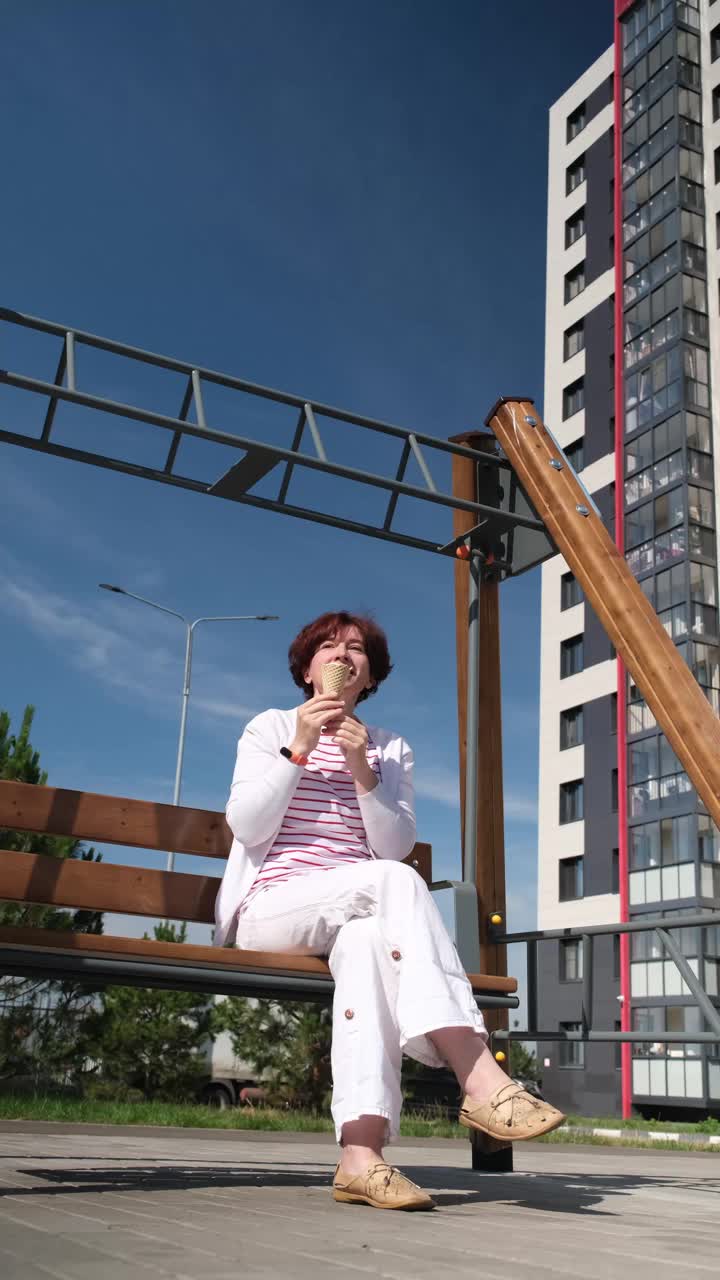 一个女人坐在城市街道的摇椅上，享受着冰淇淋蛋筒视频素材