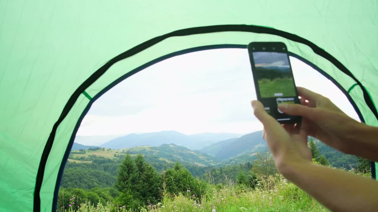 女孩用智能手机在日落时用帐篷拍下美丽的山景视频下载
