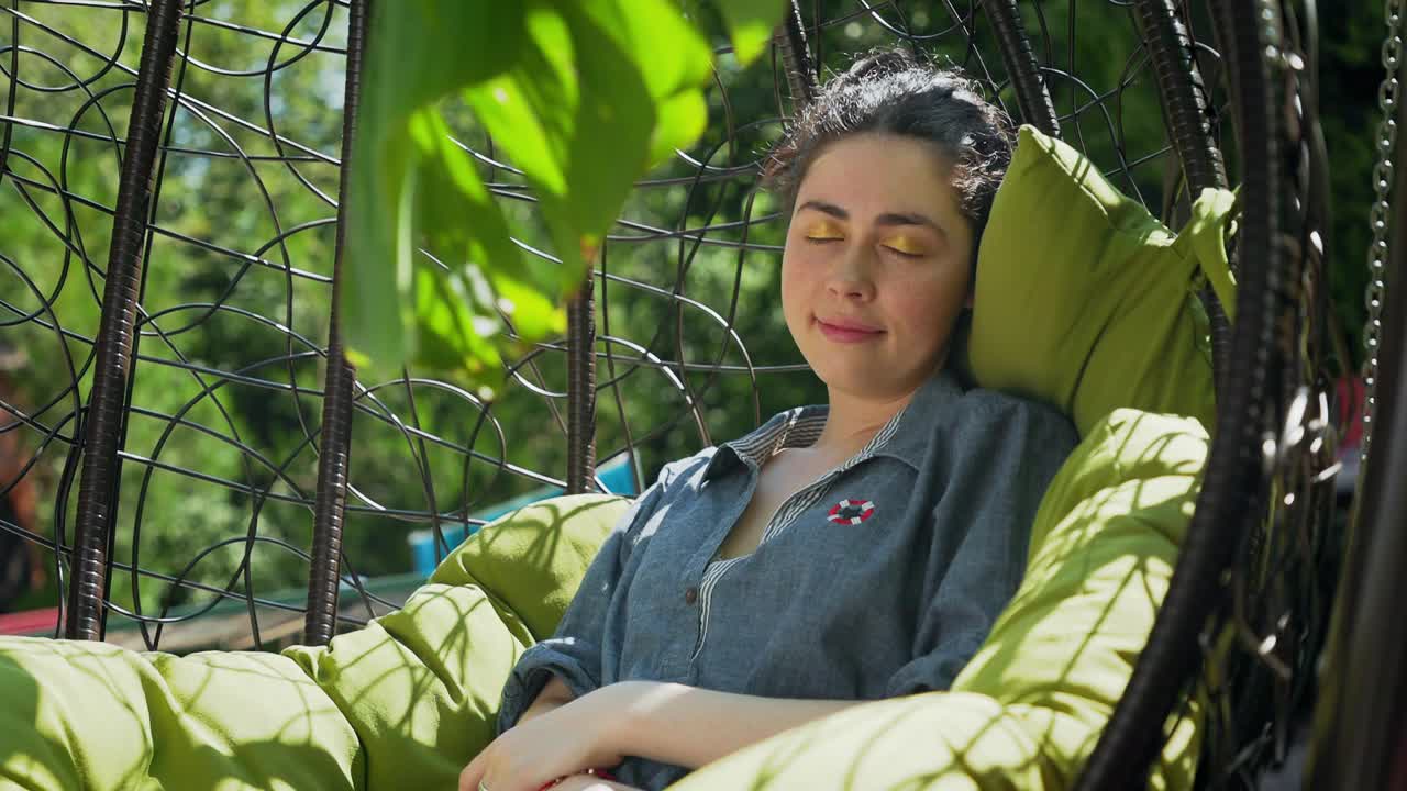 暑假。一个年轻漂亮的女人，摇晃着，睡在一张柳条椅上。真正的时间。放松和娱乐视频下载