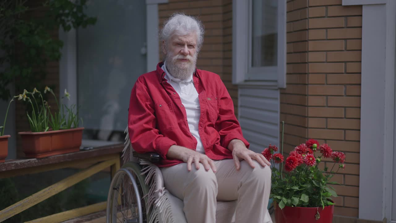 现场镜头放大到悲伤孤独的残疾老人坐在轮椅坐在阳光明媚的夏日门廊。绝望绝望的白人残疾退休老人的肖像在阳光下独自摆姿势。视频素材