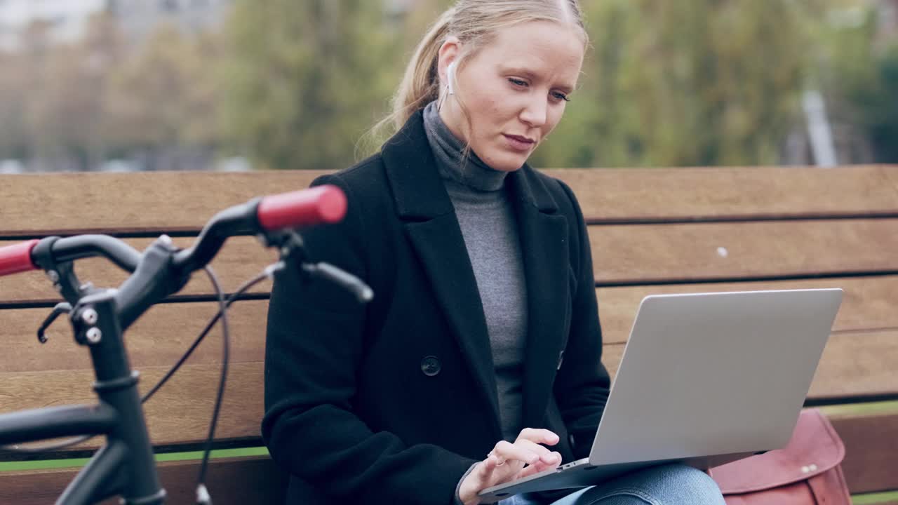 戴着耳机坐在长凳上用笔记本电脑的女人视频素材