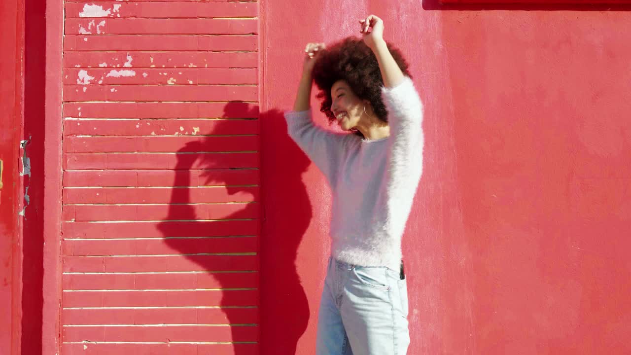 年轻女子在红墙前快乐地跳舞视频素材