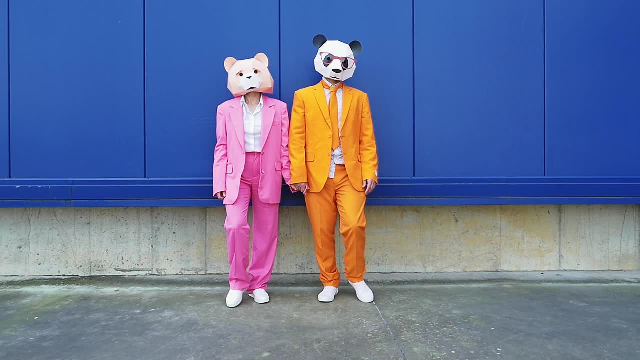 一对商业夫妇戴着动物面具，手牵手靠在蓝色的墙上视频素材