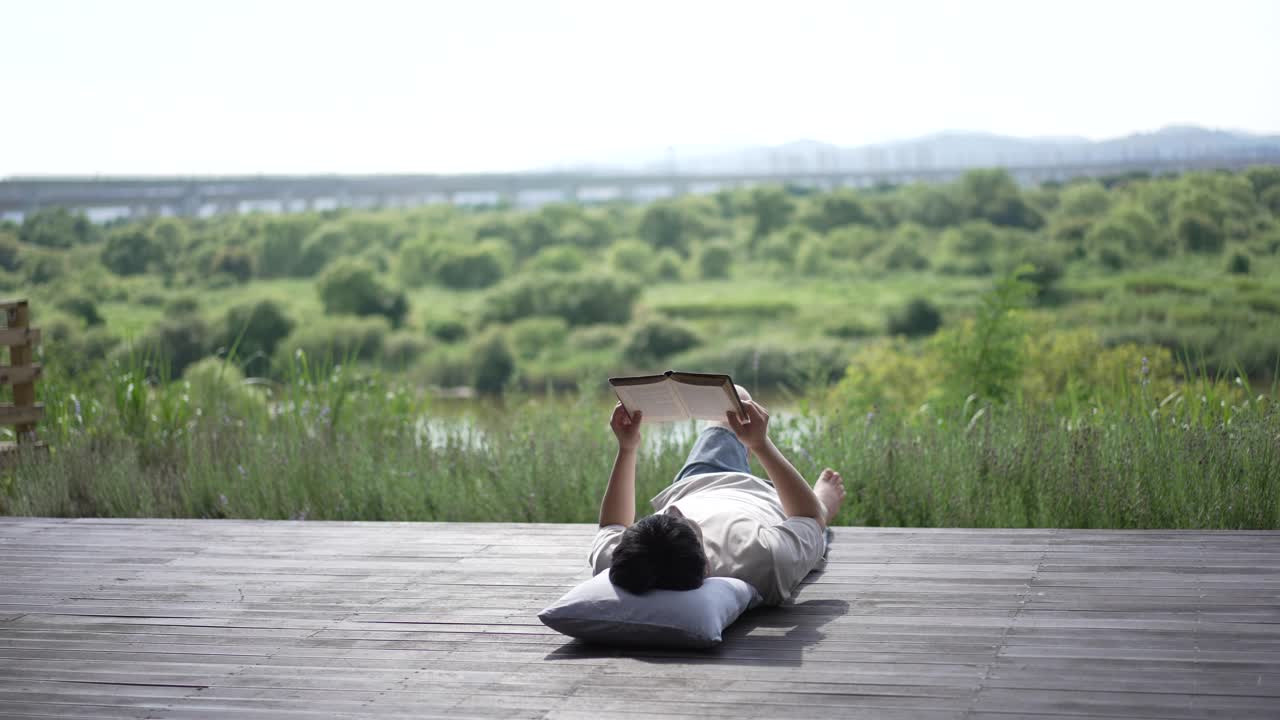 一个年轻人躺在户外甲板上看书视频下载