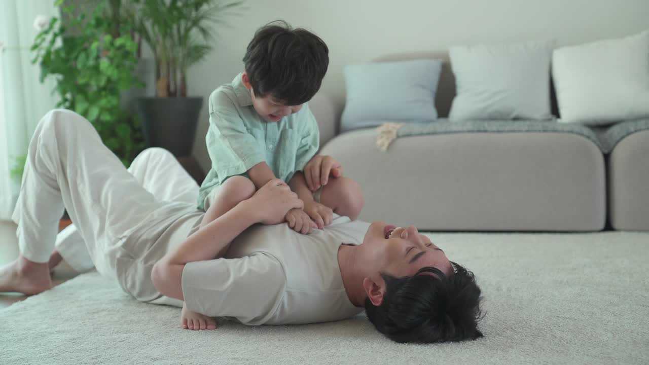 儿子坐在躺着的父亲的肚子上搔痒玩耍视频素材