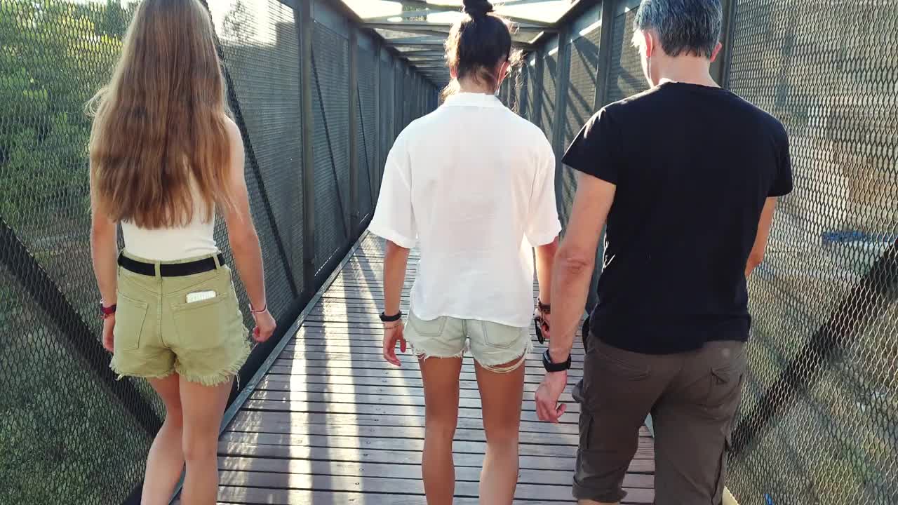 父亲一家和十几岁的女孩在阳光照耀下走在一座金属桥上视频素材