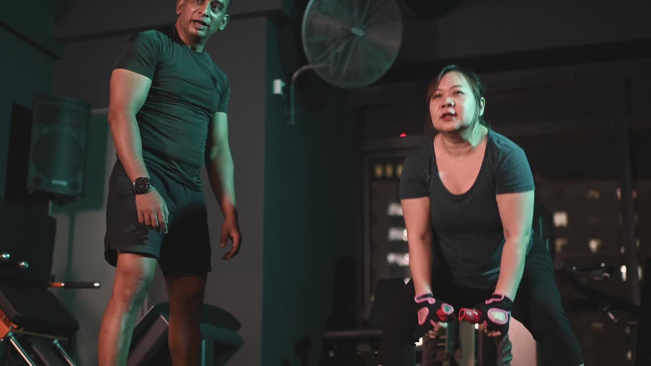 慢动作身体积极亚洲华人中，成年女子练习战斗绳在健身房与她的印度男性私人教练视频素材