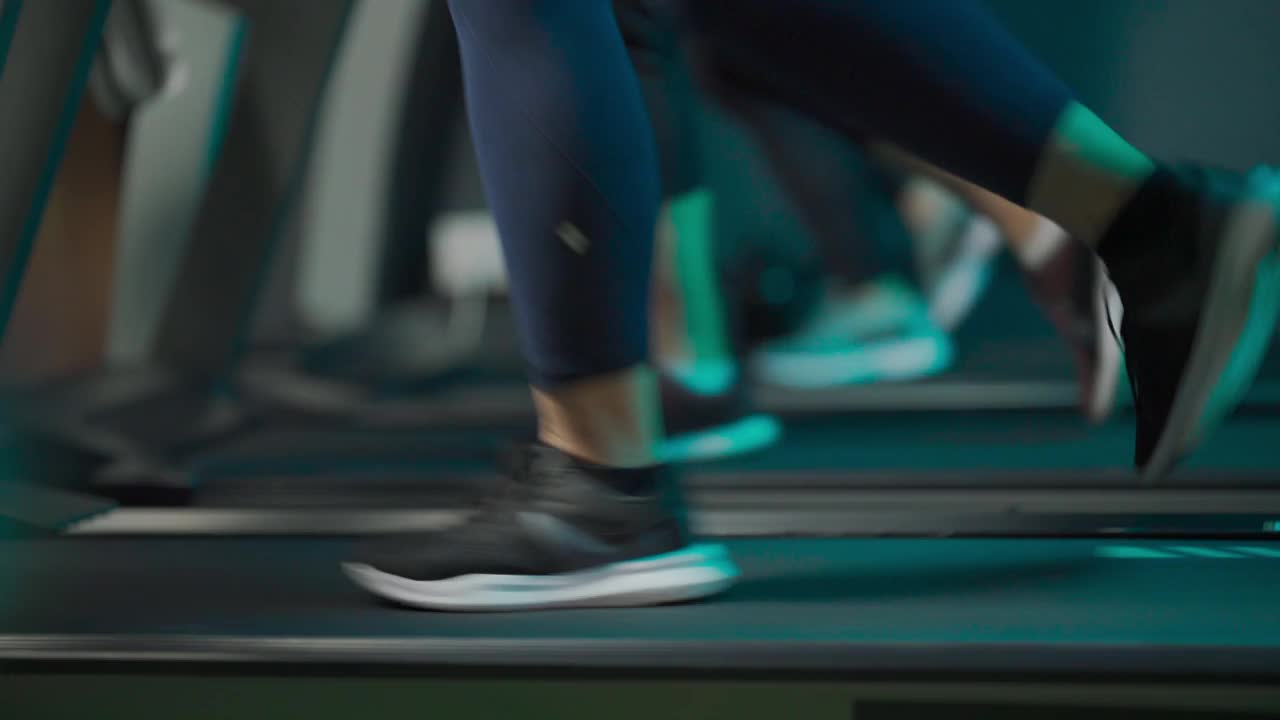 低角度侧视身体正面的女性和她的女性朋友在健身房跑步机在晚上面对城市的街灯视频下载