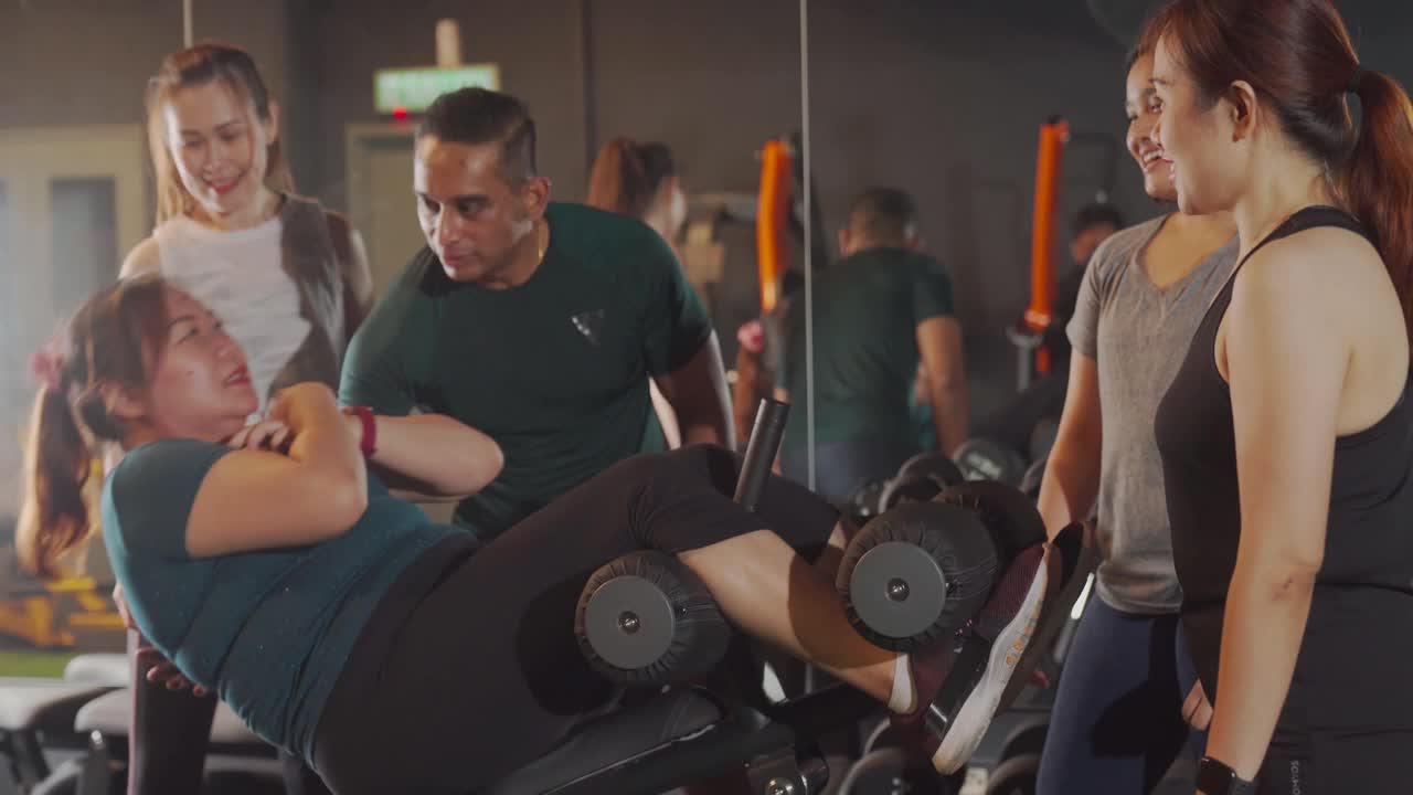 亚洲男性健身教练指导身体积极中成年女性在健身房仰卧起坐和其他女性运动员一起锻炼视频素材
