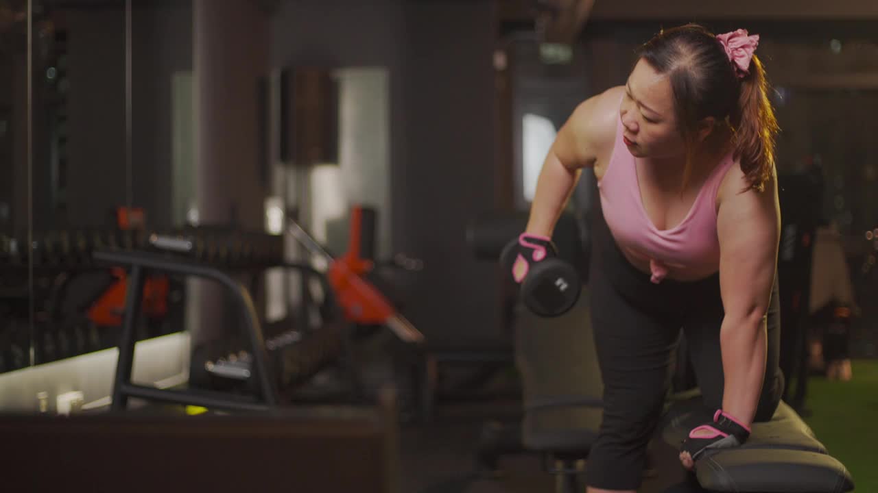 身体积极的亚洲中年女性，晚上在健身房用哑铃做弓步运动视频素材