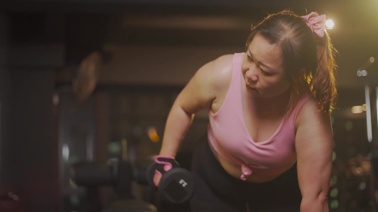 身体积极的亚洲中年妇女在健身房锻炼哑铃在一个弓步的姿势在晚上视频素材