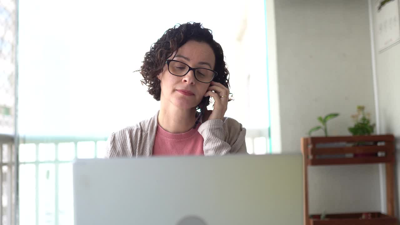 成熟的女人在家里用电话和笔记本电脑工作视频下载