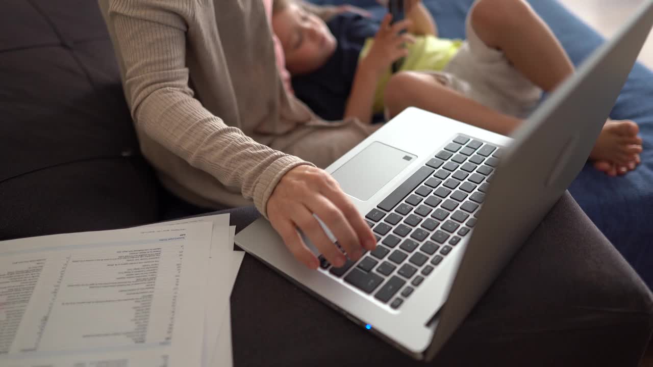 在家带着孩子坐在沙发上用笔记本电脑的女人视频素材