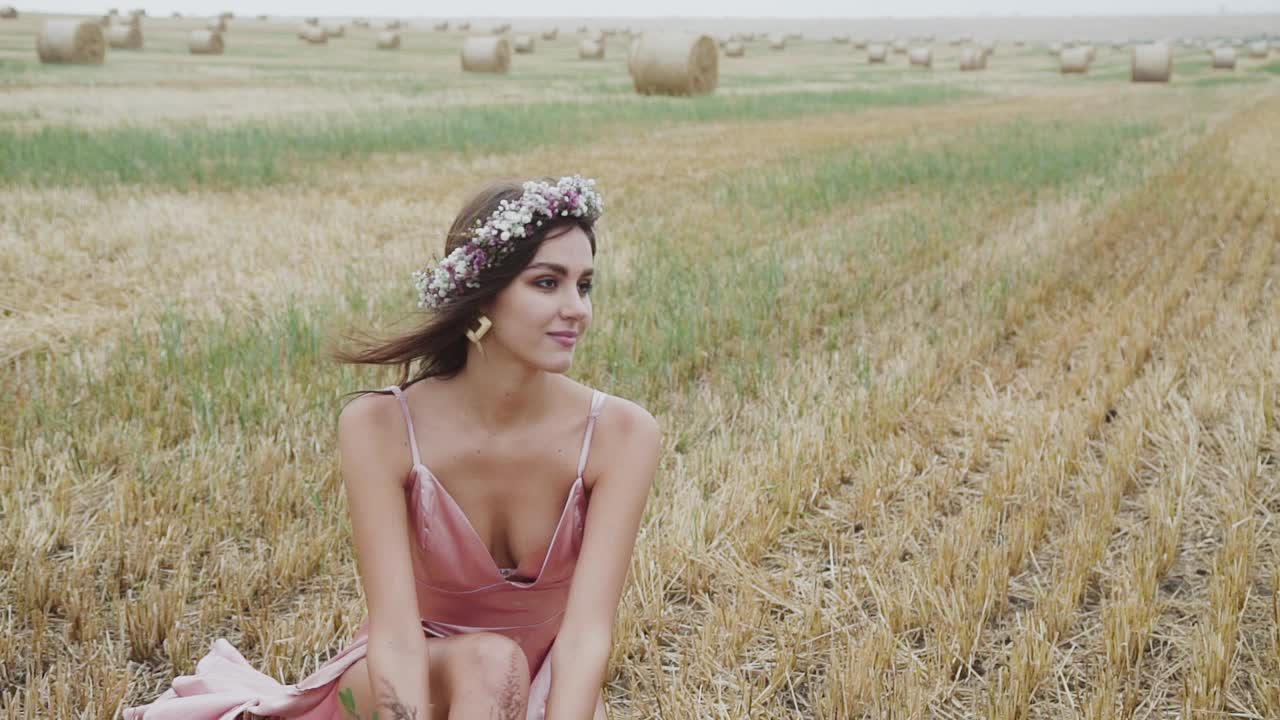 优雅的女士穿着鲜花坐在田间的麦茬上，摆着姿势视频素材